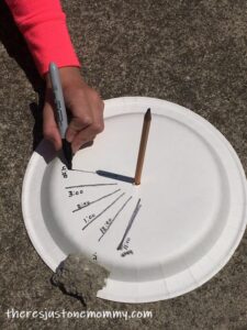 child drawing lines on paper plate sundial